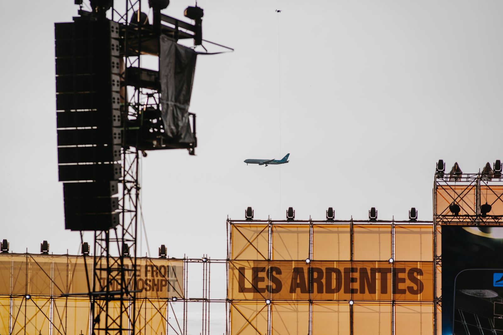 Structures scéniques et panneaux orange du festival Les Ardentes 2024, avec un avion dans le ciel